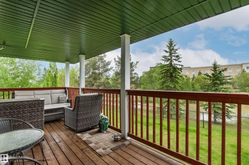 Spacious covered deck featuring wood-finish decking, white support columns, and a rich wood-stained railing - 32 Lamplight Bay, Spruce Grove, AB 