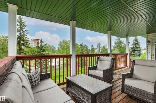 Spacious covered deck featuring wood decking, white support columns, and a rich wood railing - 32 Lamplight Bay, Spruce Grove, AB 