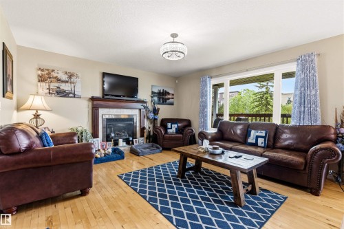 Living area featuring wood-finish flooring, a fireplace with a wood mantel and tile surround, and a large window offering exterior views - 32 Lamplight Bay, Spruce Grove, AB 