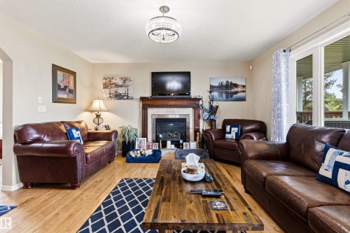 Living area featuring wood-finish flooring, a fireplace with a stone surround and wood mantel, and sliding glass doors - 32 Lamplight Bay, Spruce Grove, AB 