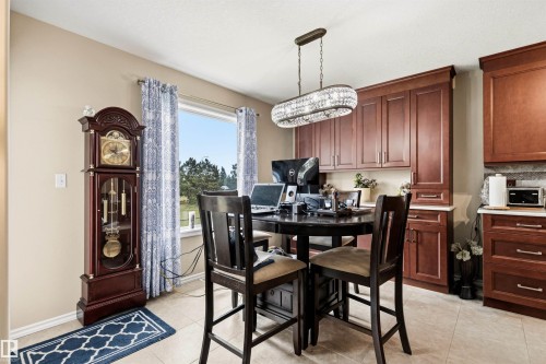 Dining area featuring a contemporary chandelier, wood-finish cabinetry, light-toned tiled flooring, and a large window - 32 Lamplight Bay, Spruce Grove, AB 