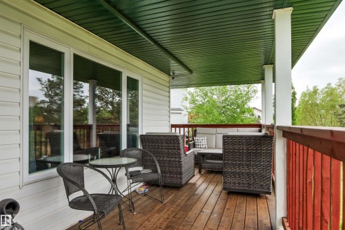 Spacious covered deck featuring wood-finish flooring, a vibrant red railing, white support columns, and a green soffit - 32 Lamplight Bay, Spruce Grove, AB 