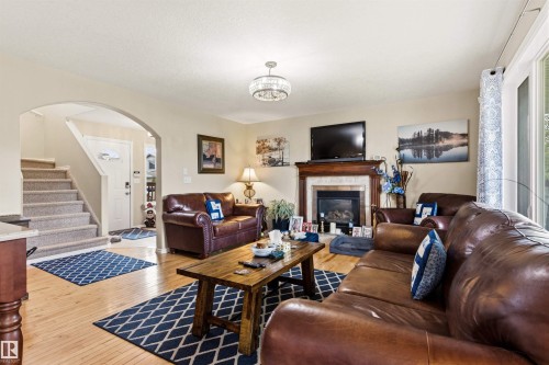 Living area featuring wood-finish flooring, a fireplace with a wood mantle and stone surround, and an arched entryway - 32 Lamplight Bay, Spruce Grove, AB 