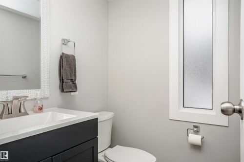 Bathroom featuring a dark vanity cabinet with white countertop, chrome faucet, white framed mirror, and a frosted privacy window - 3103 109 Street, Edmonton, AB 