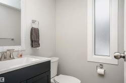 Bathroom featuring a dark vanity cabinet with white countertop, chrome faucet, white framed mirror, and a frosted privacy window - 