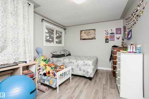 Bedroom featuring light gray walls, wood-finish flooring, and a window with white trim - 3103 109 Street, Edmonton, AB 