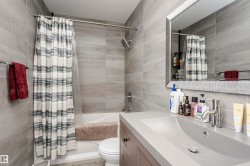 Bathroom featuring a built-in tub with a shower fixture, expansive gray tile surround, and a coordinating vanity with an integrated sink - 