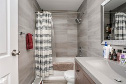 Bathroom featuring a tiled shower surround, rain shower head, integrated vanity sink, and a framed mirror - 