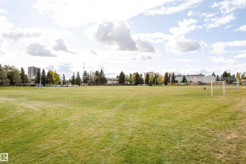 Expansive green space featuring large grassy areas, perimeter trees, and neighborhood buildings in the background - 3103 109 Street, Edmonton, AB 