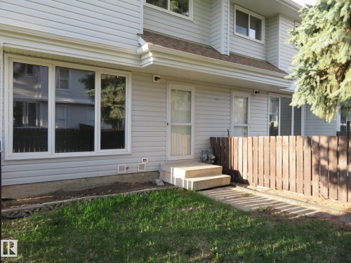 Light-toned siding exterior featuring multiple windows, a wooden privacy fence, and a concrete patio area with steps - 3103 109 Street, Edmonton, AB 