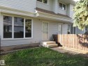 Light-toned siding exterior featuring multiple windows, a wooden privacy fence, and a concrete patio area with steps - 3103 109 Street, Edmonton, AB 