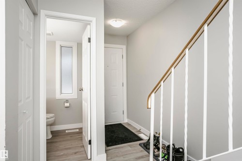 Interior hallway with light gray walls, wood-finish flooring, a white staircase with decorative balusters and a wood handrail, and a white entry door - 3103 109 Street, Edmonton, AB 