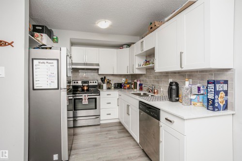 Kitchen featuring white shaker-style cabinetry, light wood-finish flooring, stainless steel appliances, and a tiled backsplash - 3103 109 Street, Edmonton, AB 