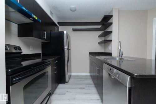 Kitchen featuring dark cabinetry, stainless steel appliances, dark countertops, and light wood-finish flooring - 108 530 Watt Boulevard, Edmonton, AB 