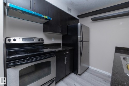 Kitchen featuring dark wood-finish cabinetry, stainless steel appliances, dark countertops, and light wood-finish flooring - 108 530 Watt Boulevard, Edmonton, AB 