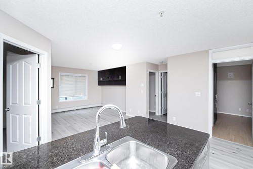 Kitchen island with a dark speckled countertop and stainless steel double basin sink with a chrome gooseneck faucet - 108 530 Watt Boulevard, Edmonton, AB 