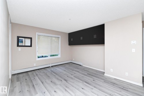 Room featuring wood-finish flooring, a white window with blinds, and built-in black wall cabinetry - 108 530 Watt Boulevard, Edmonton, AB 