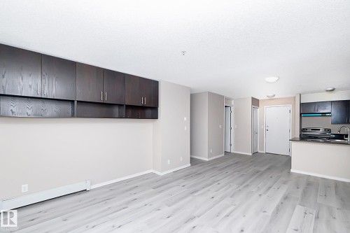 Open-concept living space featuring wood-finish flooring, neutral wall tones, and extensive dark wood-finish cabinetry - 108 530 Watt Boulevard, Edmonton, AB 