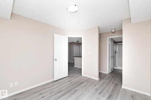 Spacious room featuring wood-finish flooring, light neutral wall paint, white trim, and a white paneled door - 108 530 Watt Boulevard, Edmonton, AB 