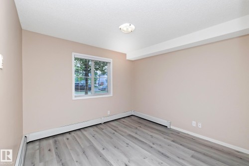 Neutral-toned room featuring a window with horizontal blinds, wood-finish flooring, and white baseboard heating - 108 530 Watt Boulevard, Edmonton, AB 