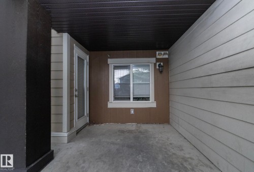 Covered concrete patio space featuring horizontal siding, a glass-paneled door, and an exterior window with trim - 108 530 Watt Boulevard, Edmonton, AB 