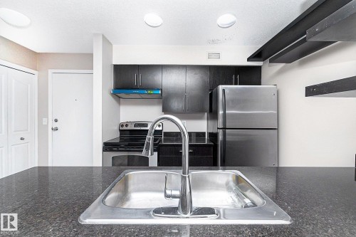 Kitchen featuring dark cabinetry, stainless steel appliances, a chrome faucet, and dark countertops - 108 530 Watt Boulevard, Edmonton, AB 