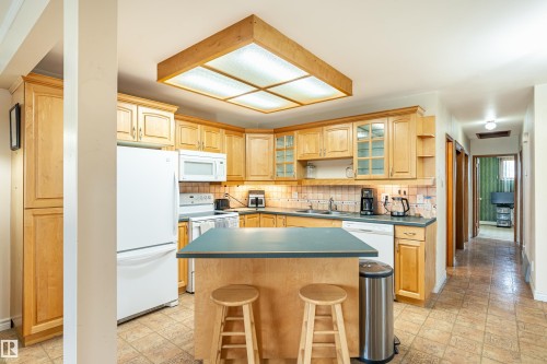 Kitchen featuring a central island, light wood cabinetry, tiled flooring, and a patterned backsplash - 9011 60 Street, Edmonton, AB 