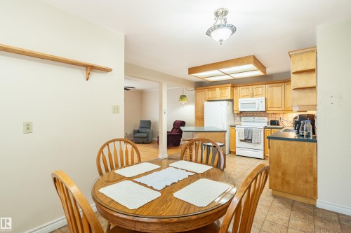 Kitchen and dining area featuring warm wood-finish cabinetry, white appliances, and a tiled floor - 9011 60 Street, Edmonton, AB 