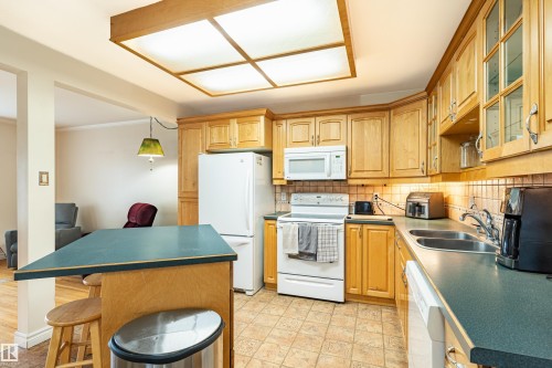 Kitchen featuring wood cabinetry with glass-front accents, laminate countertops, a tile backsplash, and a double-basin stainless steel sink - 9011 60 Street, Edmonton, AB 