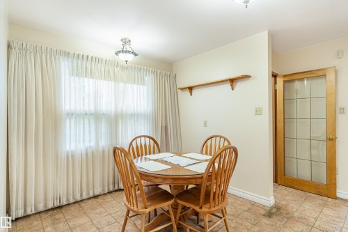 Dining area featuring a central window with sheer and blackout curtains, tiled flooring, an overhead semi-flush mount light fixture, and a wooden shelf - 9011 60 Street, Edmonton, AB 