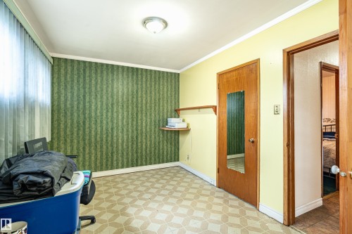 Interior room featuring a patterned accent wall, light-toned vinyl flooring, and a single window with vertical blinds - 9011 60 Street, Edmonton, AB 