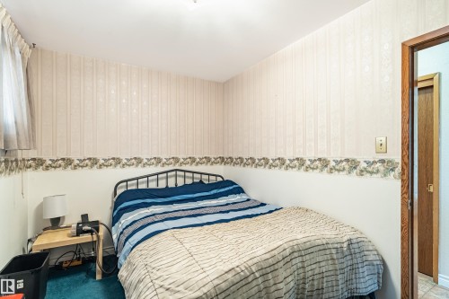 Bedroom featuring patterned wallpaper with floral border, wood-finish door frame, and ceiling-mounted light fixture - 9011 60 Street, Edmonton, AB 