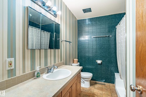 Bathroom featuring a built-in vanity with an integrated sink, chrome-finish faucet, and a stone-finish countertop - 9011 60 Street, Edmonton, AB 