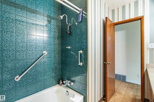 Bathroom featuring a white bathtub with a tile surround, dual shower heads, and multiple grab bars - 9011 60 Street, Edmonton, AB 