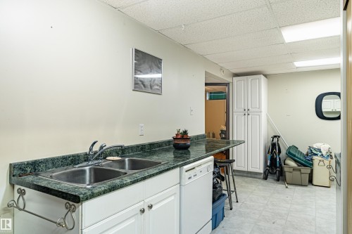 Utility area featuring a double basin sink, green patterned countertop, white cabinetry with silver hardware, and a built-in dishwasher - 9011 60 Street, Edmonton, AB 