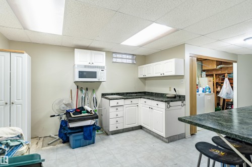 Kitchenette featuring white cabinetry, dark speckled countertops, an over-range microwave, a sink, and tile flooring - 9011 60 Street, Edmonton, AB 