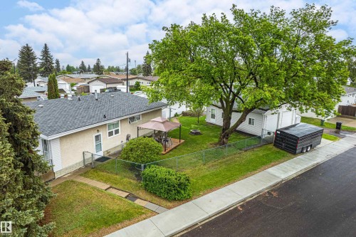 Expansive rear yard featuring a wooden deck, mature shade tree, and detached garage with dual doors - 9011 60 Street, Edmonton, AB 