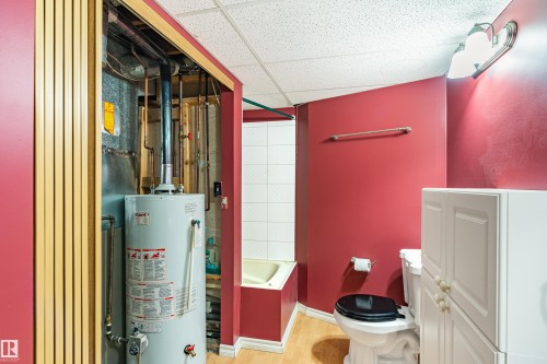 Water heater and exposed utility lines, white toilet, white wall-mounted cabinet, light wood-finish flooring, and white wall tiles - 9011 60 Street, Edmonton, AB 