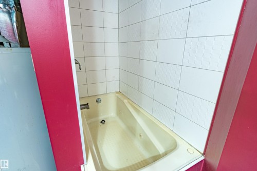 Bathtub with white tile surround, featuring textured and smooth tiles - 9011 60 Street, Edmonton, AB 