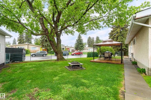 Spacious side yard featuring a mature tree, chain link fencing, a dedicated concrete pathway, a built-in fire pit, and a raised wooden deck with a gazebo - 9011 60 Street, Edmonton, AB 
