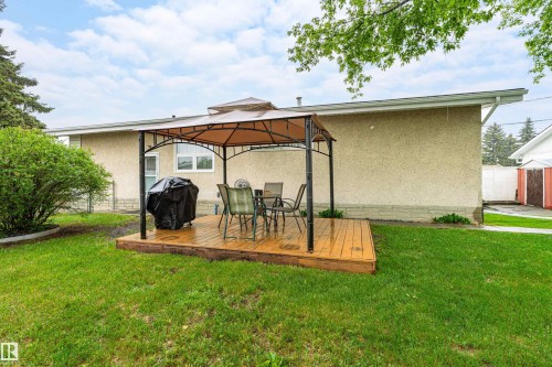 Expansive backyard featuring a wood-finish deck with a gazebo structure, surrounded by green lawn and mature landscaping - 9011 60 Street, Edmonton, AB 