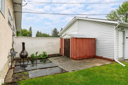 Expansive grassy yard featuring a concrete patio, white chain-link fence, and a red storage shed - 9011 60 Street, Edmonton, AB 