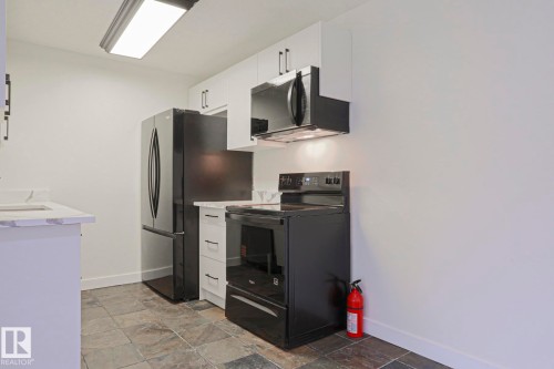 Kitchen featuring slate-look floor tile, white cabinetry with dark hardware, stone-look countertops, and a full suite of black kitchen appliances - 205 14903 92 Avenue Nw, Edmonton, AB 