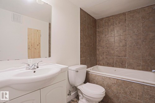 Bathroom featuring a white integrated sink vanity with chrome faucet, a standard toilet, and a bathtub with full-height tiled surround - 205 14903 92 Avenue Nw, Edmonton, AB 