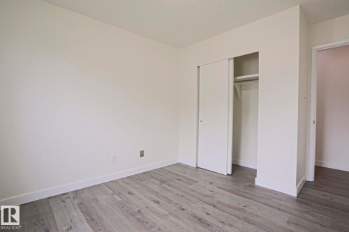 Room featuring neutral wall tones, wood-finish flooring, white baseboards, and a closet with sliding doors and interior shelving - 205 14903 92 Avenue Nw, Edmonton, AB 