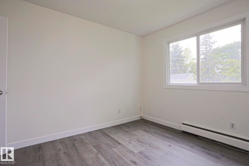 Bright room featuring light gray wood-finish flooring, white baseboards, and a large sliding window - 205 14903 92 Avenue Nw, Edmonton, AB 