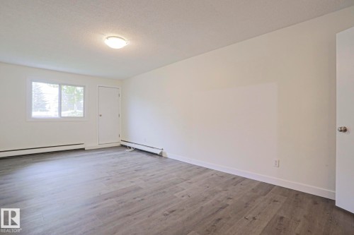 Spacious room featuring light gray wood-finish flooring, white baseboards, and a neutral wall color - 205 14903 92 Avenue Nw, Edmonton, AB 