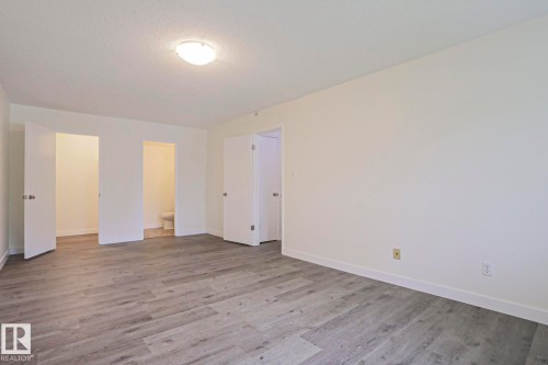 Spacious room featuring wide plank wood-finish flooring, white baseboards, and a neutral wall color - 205 14903 92 Avenue Nw, Edmonton, AB 