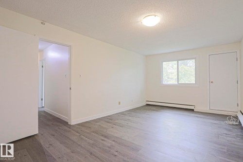 Spacious room featuring wood-finish flooring, white baseboards, and neutral wall paint - 205 14903 92 Avenue Nw, Edmonton, AB 