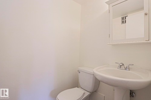 Pedestal sink with chrome faucet, toilet, and mirrored medicine cabinet - 205 14903 92 Avenue Nw, Edmonton, AB 